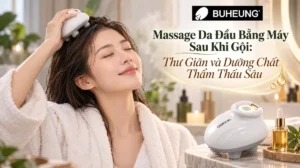Người phụ nữ thư giãn với máy massage đầu trên tóc ẩm sau khi gội, gương mặt thoải mái tận hưởng sự thẩm thấu dưỡng chất cho tóc và da đầu.